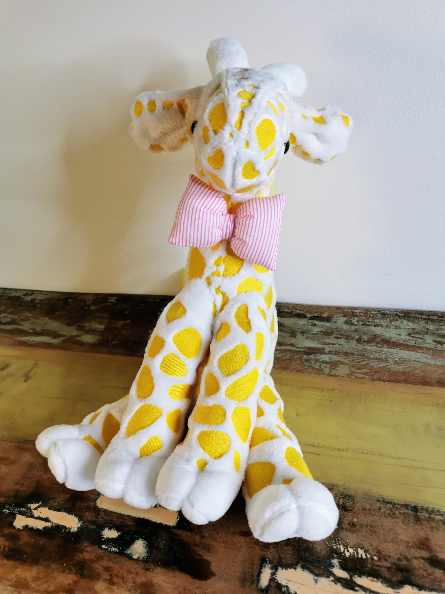 Seated Baby Giraffe plush, embroidered cuddling giraffe toy in white plush with bright yellow embroidery, pink stripe bow