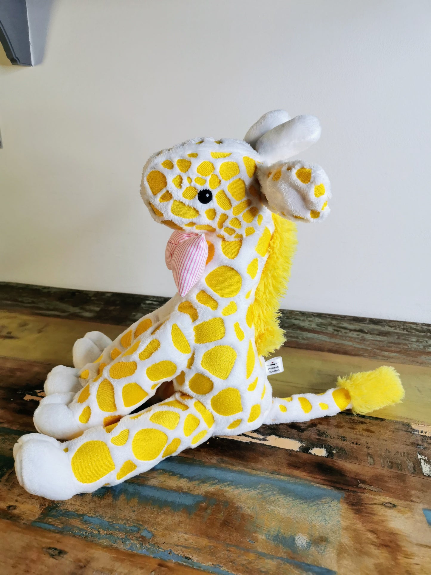 Seated Baby Giraffe plush, embroidered cuddling giraffe toy in white plush with bright yellow embroidery, pink stripe bow