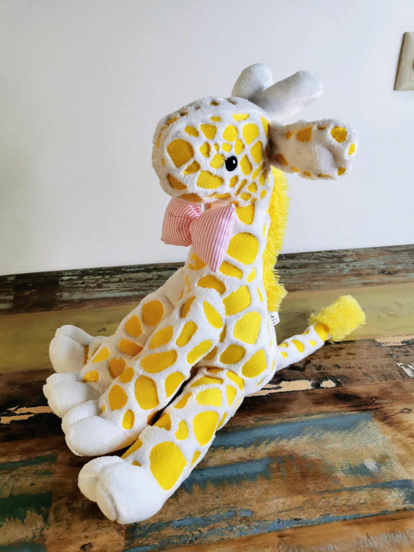 Seated Baby Giraffe plush, embroidered cuddling giraffe toy in white plush with bright yellow embroidery, pink stripe bow