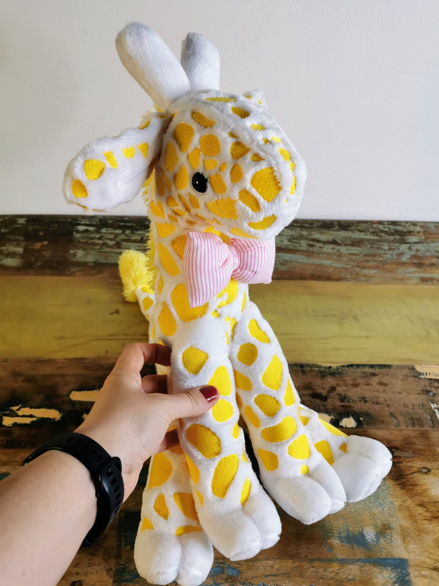Seated Baby Giraffe plush, embroidered cuddling giraffe toy in white plush with bright yellow embroidery, pink stripe bow