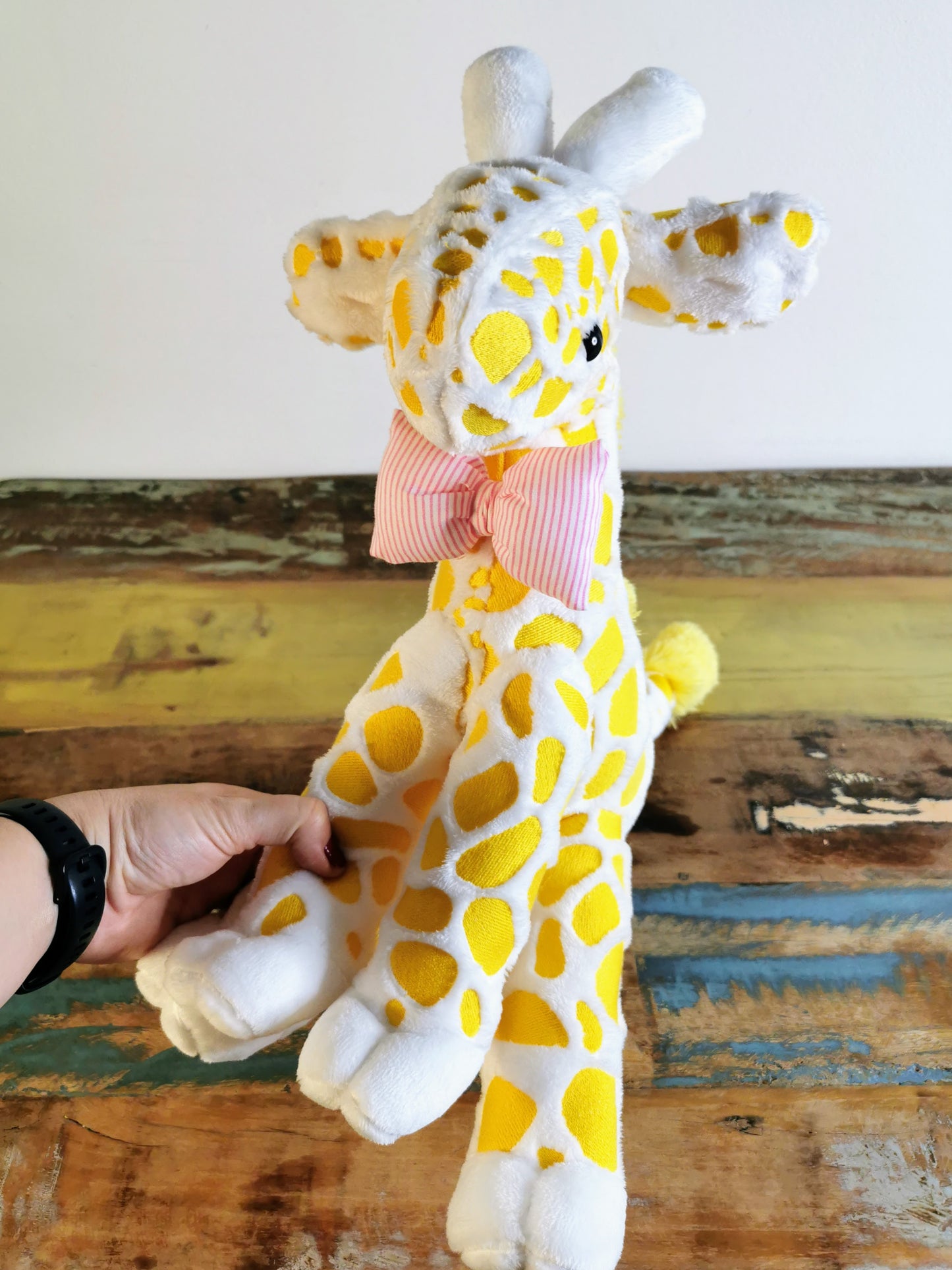 Seated Baby Giraffe plush, embroidered cuddling giraffe toy in white plush with bright yellow embroidery, pink stripe bow