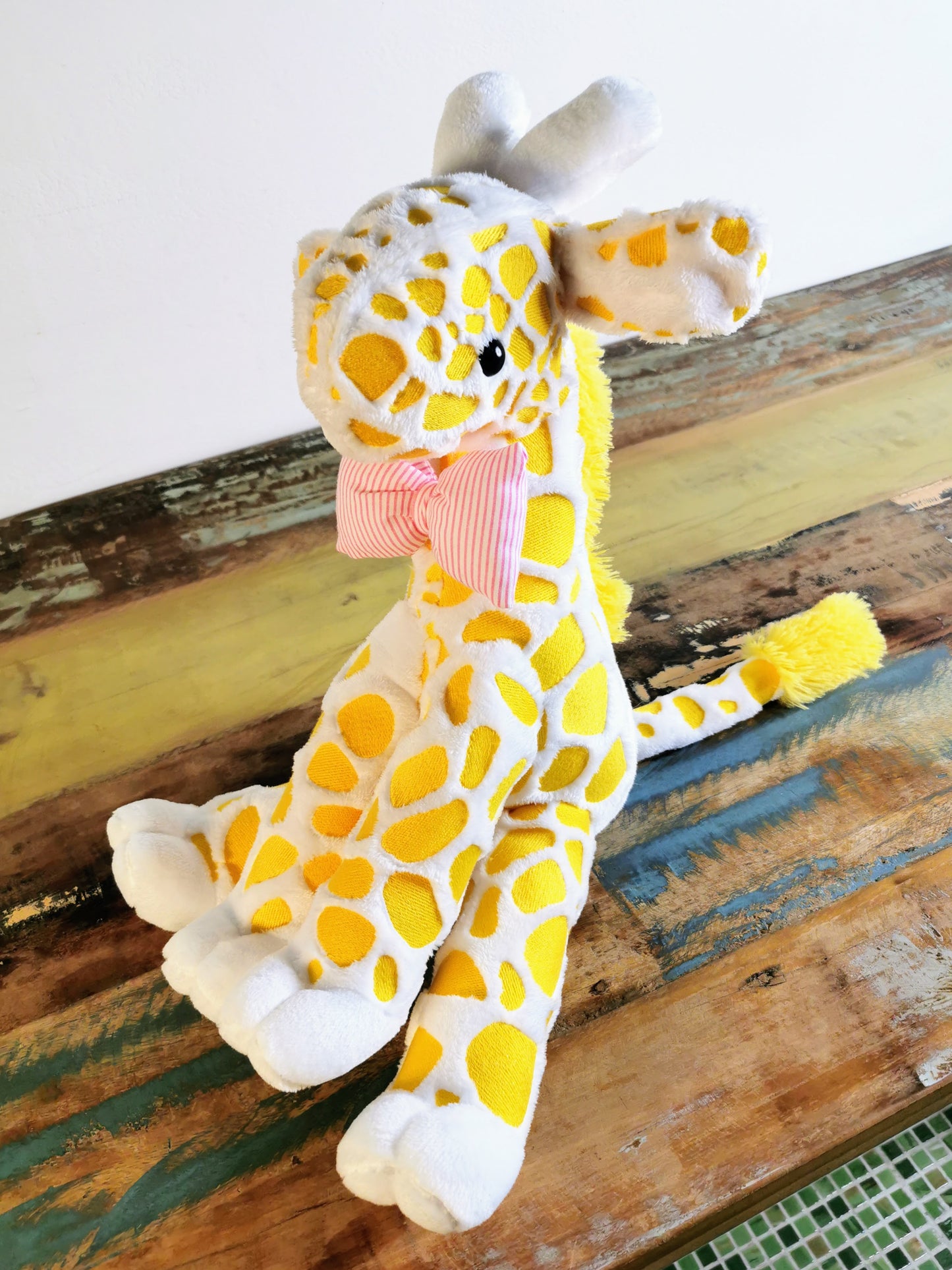 Seated Baby Giraffe plush, embroidered cuddling giraffe toy in white plush with bright yellow embroidery, pink stripe bow