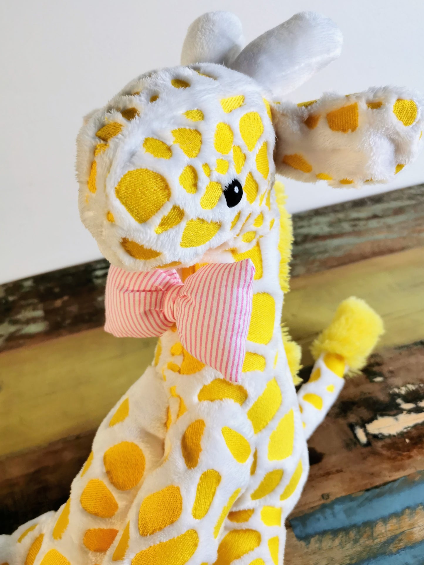Seated Baby Giraffe plush, embroidered cuddling giraffe toy in white plush with bright yellow embroidery, pink stripe bow