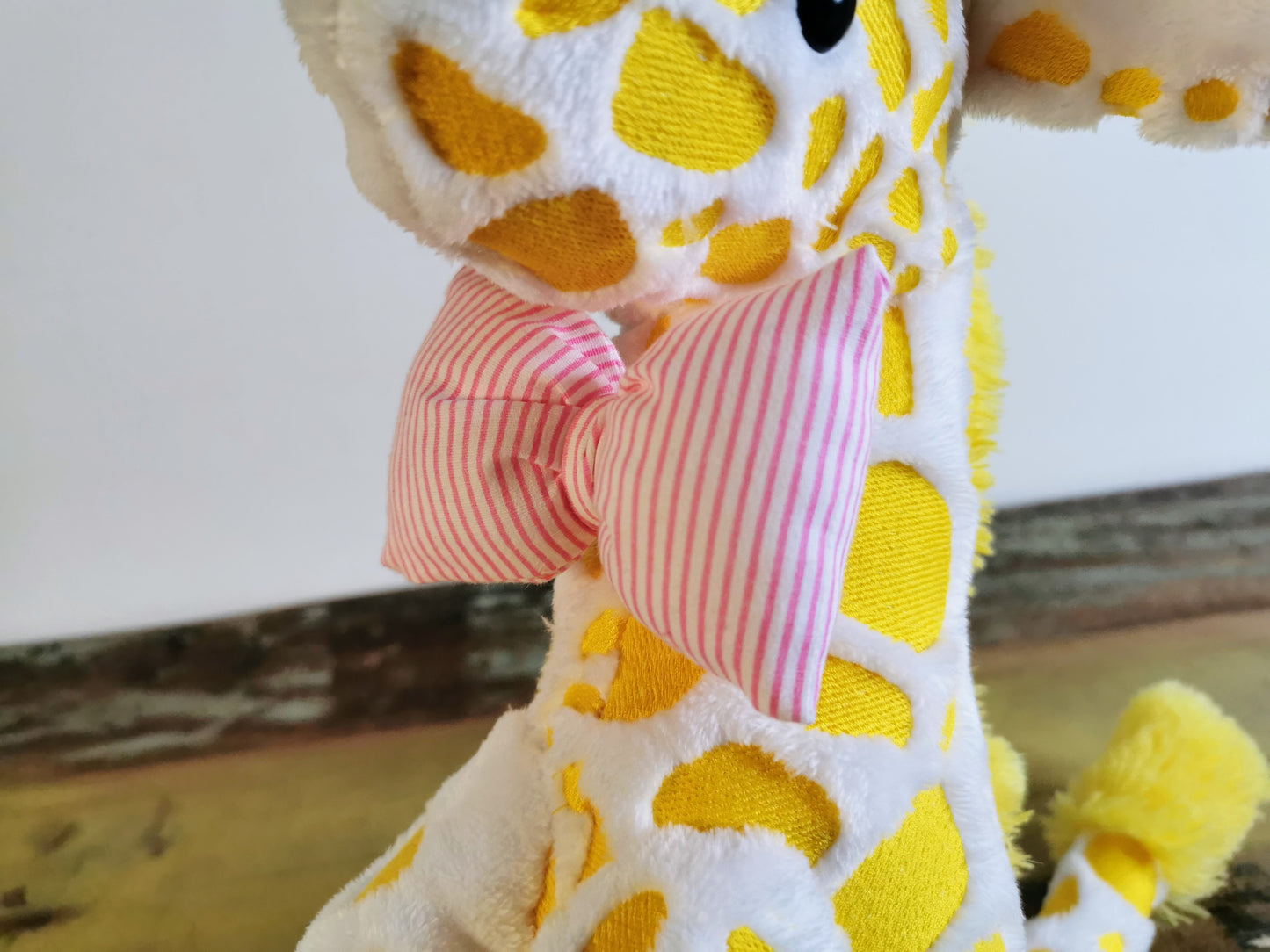 Seated Baby Giraffe plush, embroidered cuddling giraffe toy in white plush with bright yellow embroidery, pink stripe bow