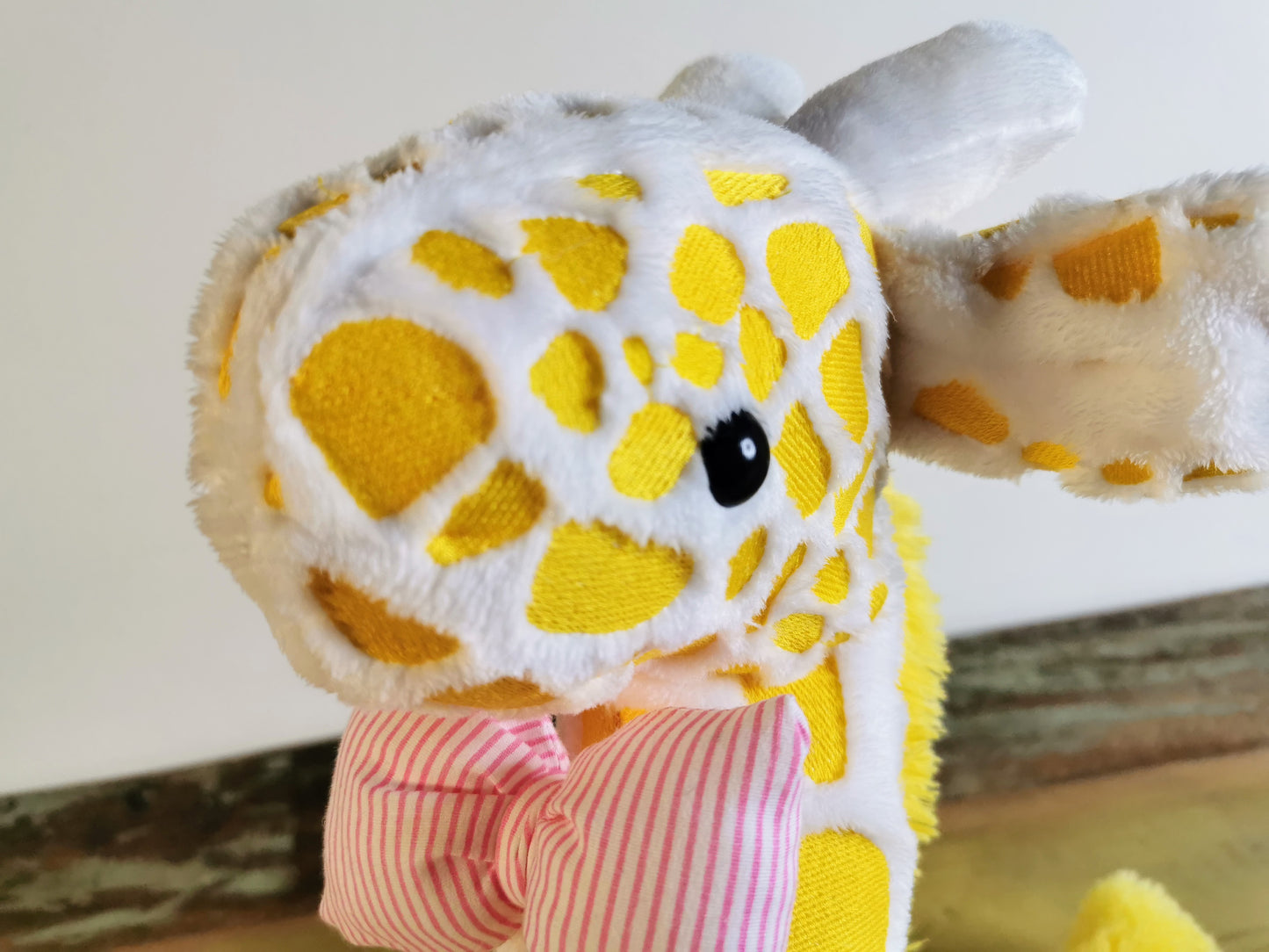 Seated Baby Giraffe plush, embroidered cuddling giraffe toy in white plush with bright yellow embroidery, pink stripe bow