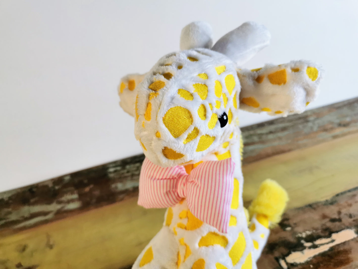 Seated Baby Giraffe plush, embroidered cuddling giraffe toy in white plush with bright yellow embroidery, pink stripe bow