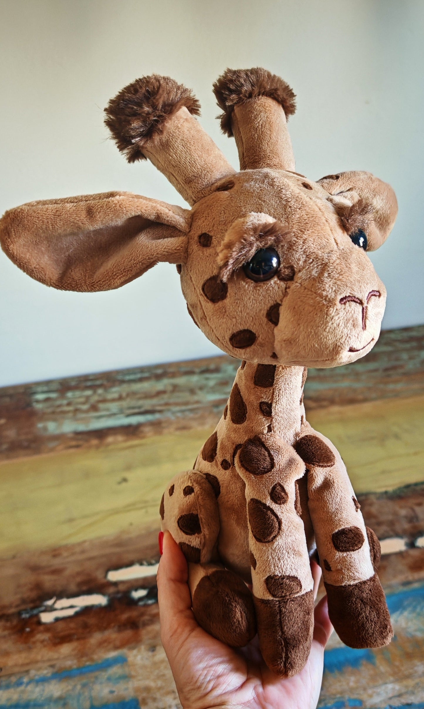 Plush giraffe toy held in a hand against a wooden background