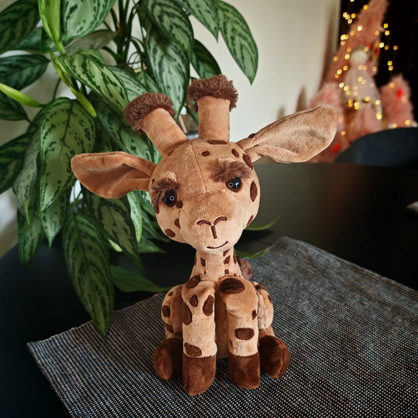 Plush giraffe toy on a textured surface with plants in the background