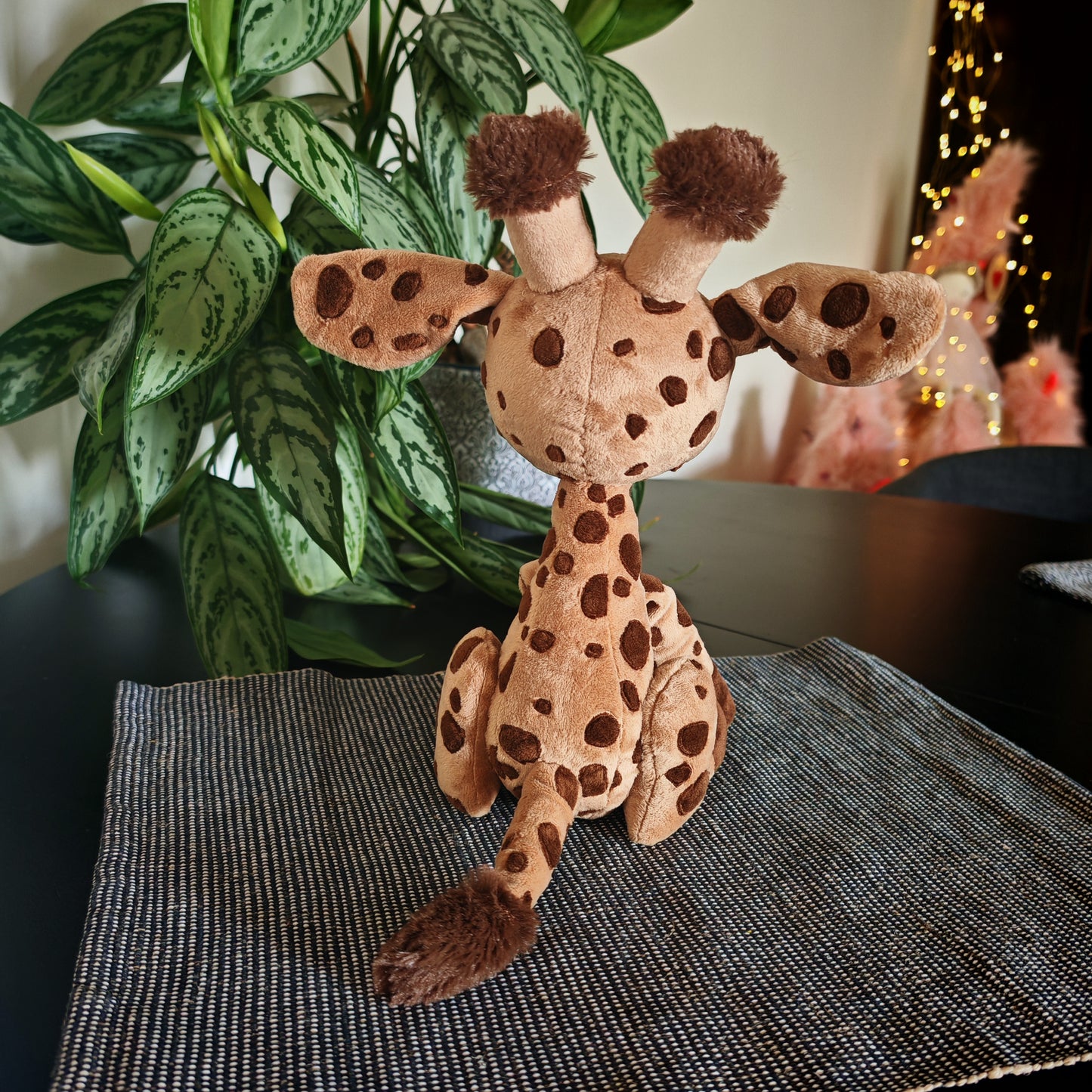 Plush giraffe toy on a textured surface with a plant in the background