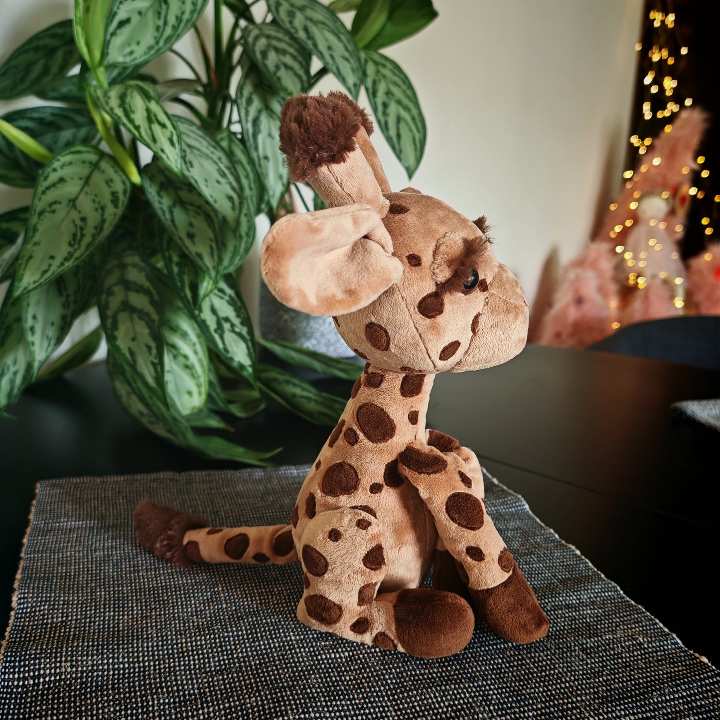 Plush giraffe toy on a textured surface with a plant and blurred lights in the background
